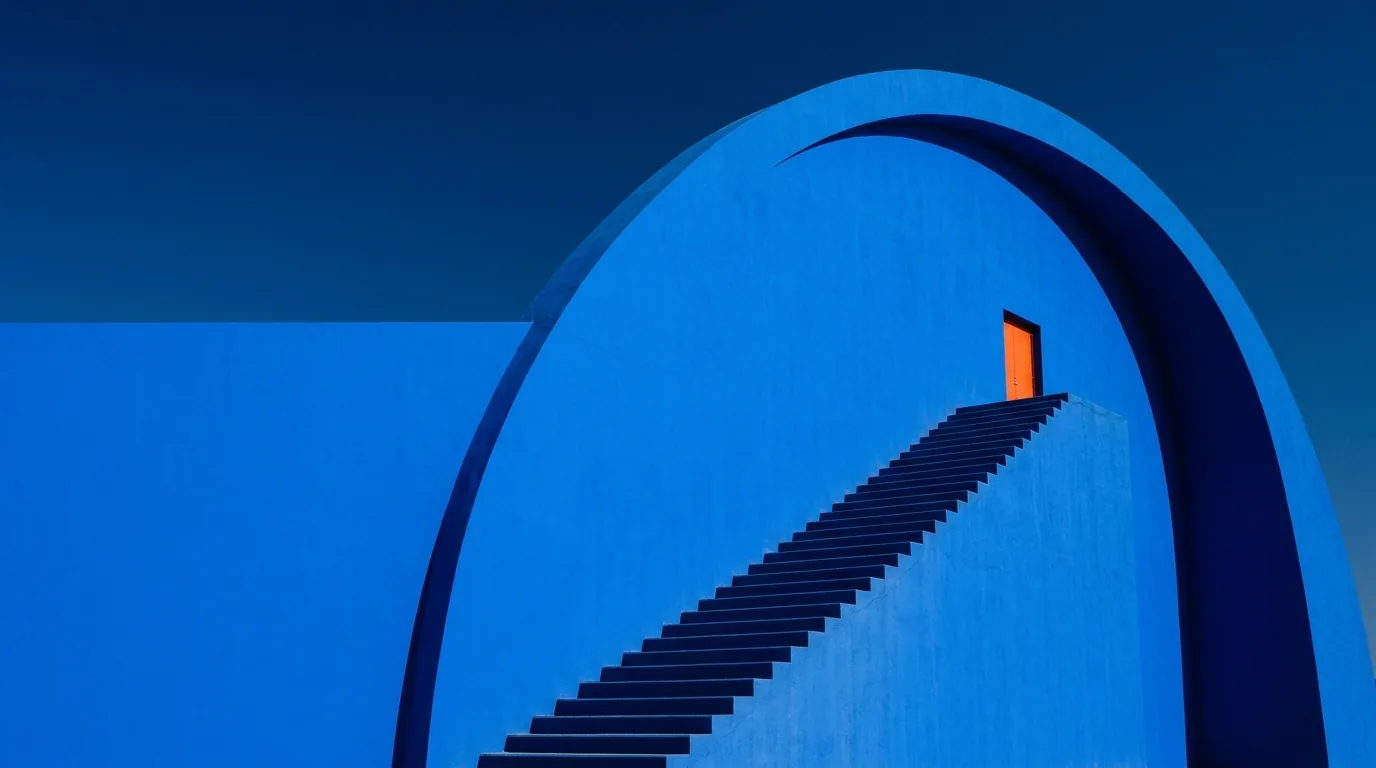 Gran arco azul con una escalera que sube hasta una puerta naranja