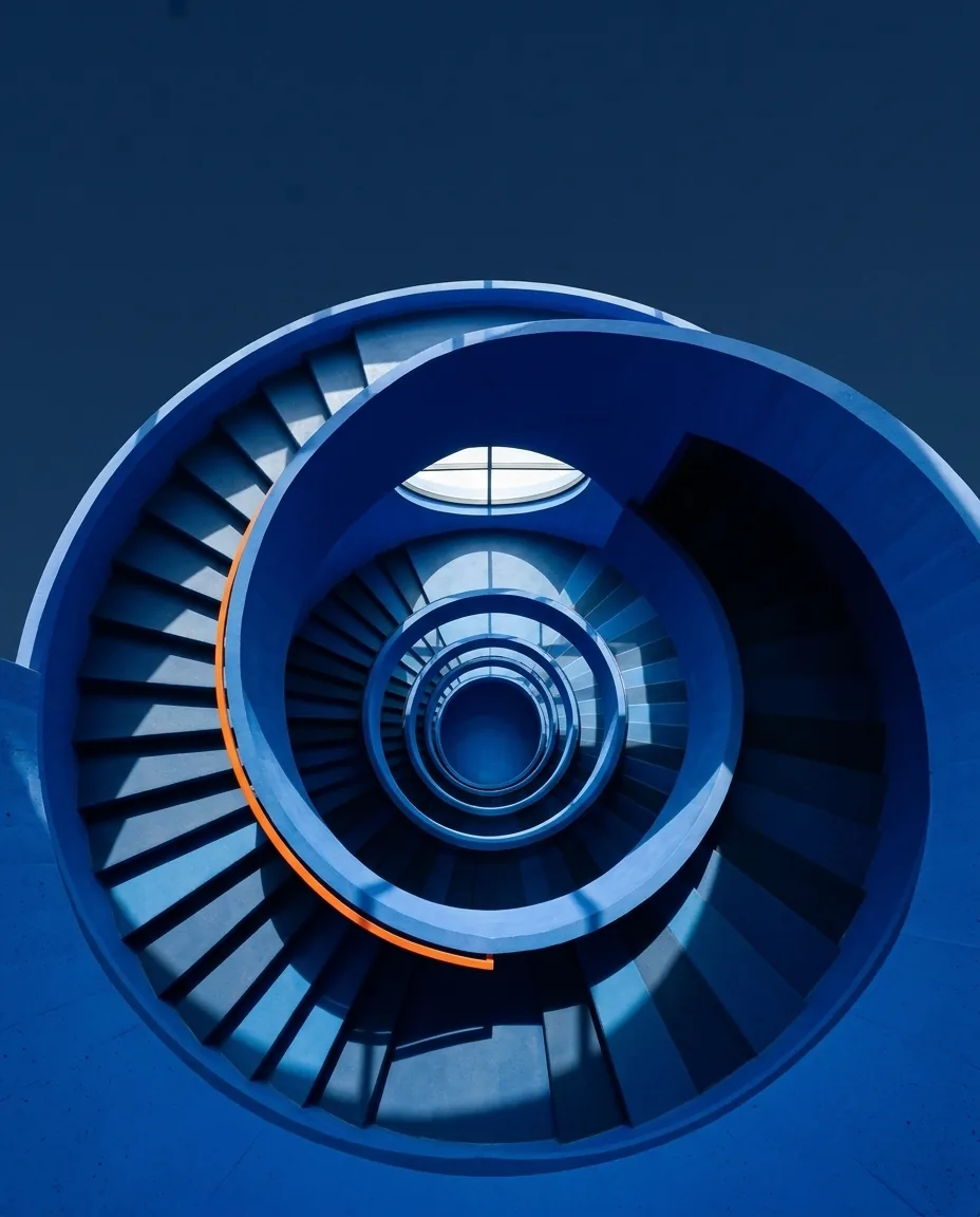 Escalera de caracol azul vista desde arriba con un tramo de barandilla naranja