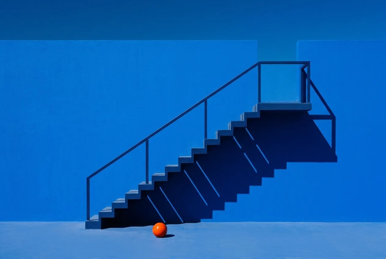 Escalera azul con barandilla y una pelota naranja al pie