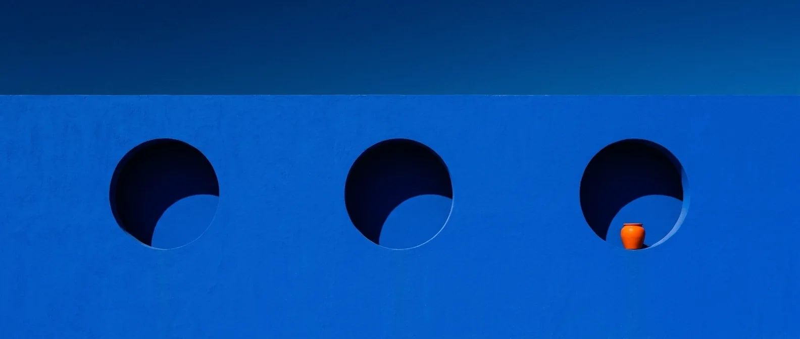 Muro azul con tres ventanas redondas y una maceta naranja
